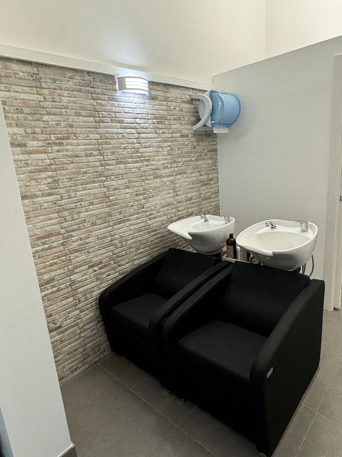 Area lavaggio con due lavatesta bianchi e poltrone nere davanti a una parete in mattoncini chiari