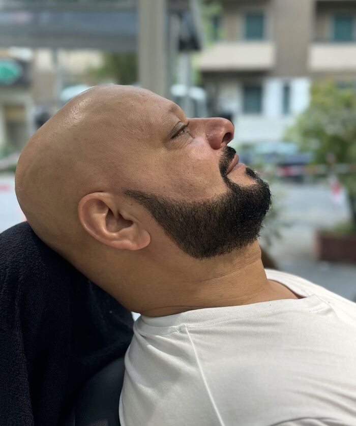 Uomo con la testa rasata e la barba scura definita, ritratto di profilo