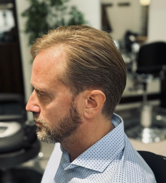 Uomo di profilo con capelli castani pettinati di lato e barba corta, in camicia azzurra