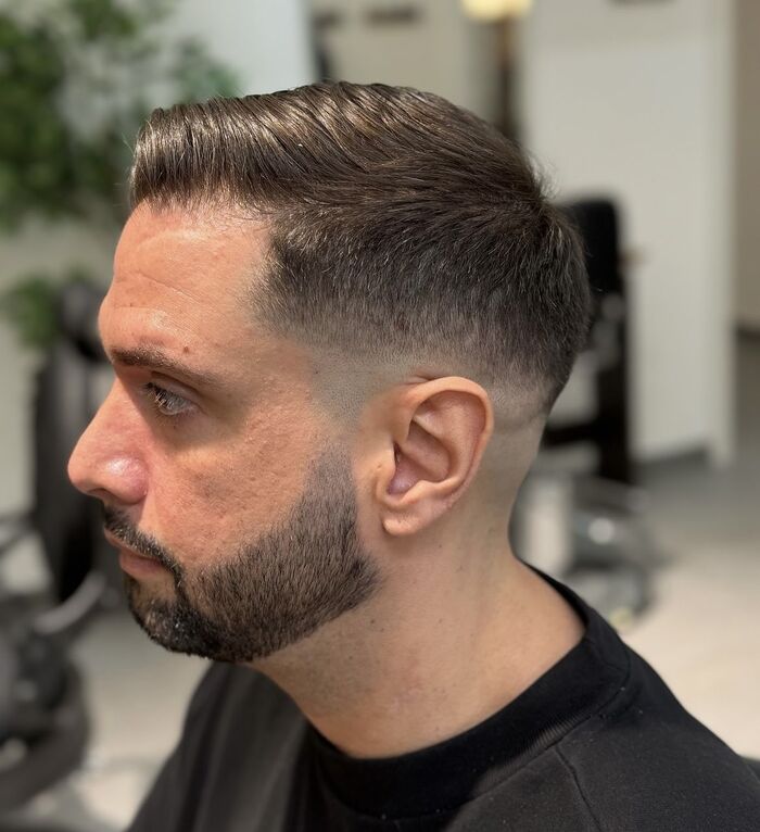 Uomo di profilo con sfumatura corta sui lati, capelli pettinati all'indietro e barba curata