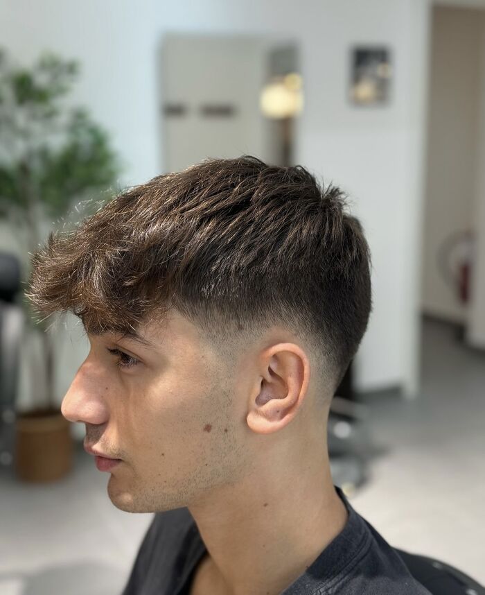 Ragazzo di profilo con sfumatura sui lati e capelli mossi lunghi sulla fronte