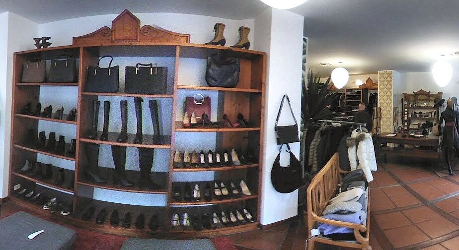 Interno del negozio: libreria in legno con borse, stivali e décolleté, pavimento in cotto e appendiabiti